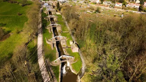 Canal and Rivers Trust A birds-eye view of five canal locks in a row. Either side of the canal is green field and bogs