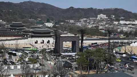 Getty Images Workers set up the stage (C) for the comeback concert of K-pop boy group BTS in front of Gwanghwamun Gate (L), the main gate of Gyeongbokgung Palace, in Seoul on March 19, 2026. 