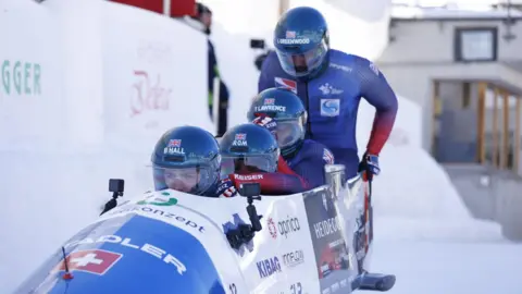 Team GB Four men in a bobsleigh. They are all wearing blue overalls.