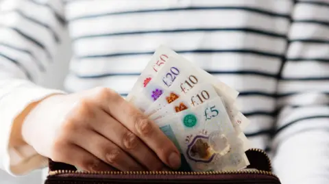 A hand putting British pound notes into a purse. The person is wearing a white and black striped top.