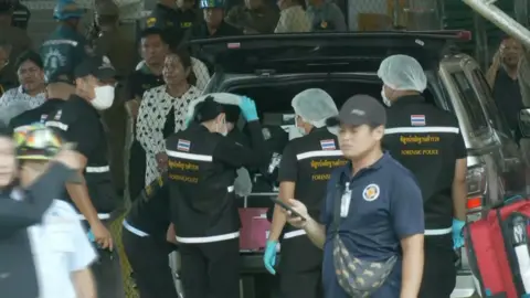 A person in blue scrubs puts on PPE from the trunk of a vehicle.