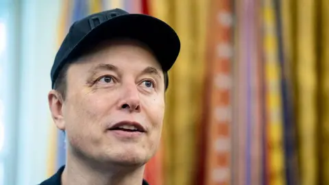 Elon Musk at the White House on 31 May on his last day, wearing a black baseball cap in the Oval Office.