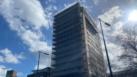 St Francis Tower with scaffolding around it. The photo is taken looking up at the building with a blue sky behind.