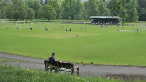 Jim Barton A man on a bench looks down over a football field in the distance with a distinctive green stand