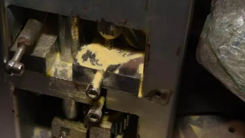 Essex Police A metal pill pressing machine with traces of white/yellow powder on some of the surfaces