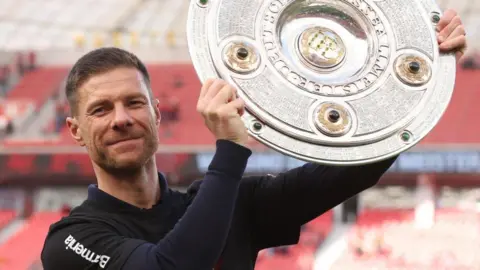 Bayer Leverkusen head coach Xabi Alonso hold aloft the German Bundesliga trophy in 2024