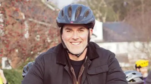 LDRS A man with a black bike helmet and black coat smiles at the camera.