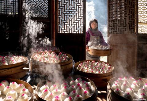 A woman entering a room to add her latest creation to a mountain of steaming dim sum, prepared as part of a feast to celebrate Chinese New Year.