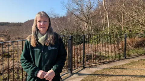 Gaynor Kerry standing in front of a fenced-off peatland area on a sunny day.