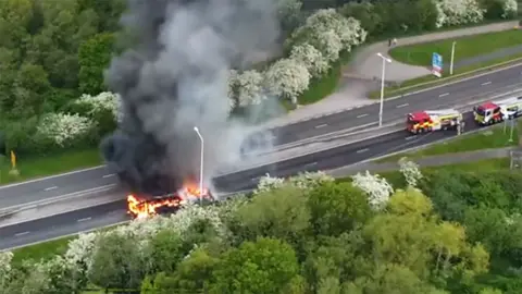 Aerial view of bus on fire there are two fire engines near by