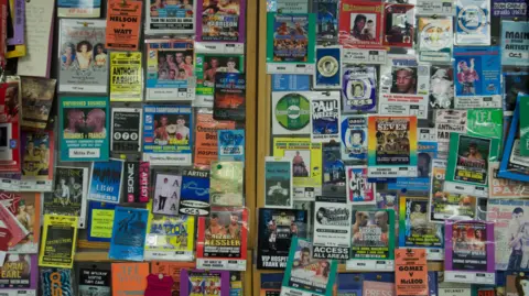 More than 100 multi-colour security pass badges hanging on a wall in an office. The badges are from music and boxing events.