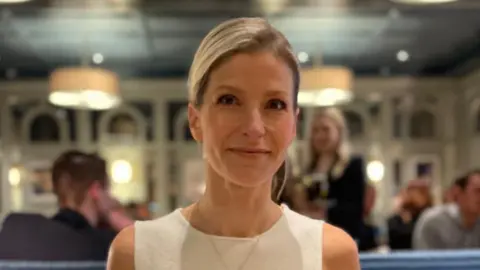 Supplied A woman sits in a restaurant - she is wearing a cream, sleeveless top and has blond hair. She is smiling at the camera.
