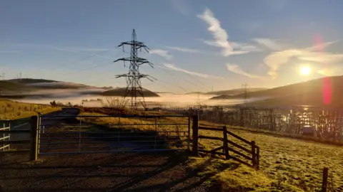 Tim Gandy Some late autumn sunshine on a south of Scotland hillside with an electricity pylon in the foreground and wind turbines in the distance