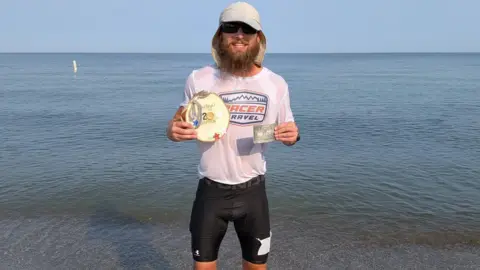 Buckeye 200/Facebook Kelly holds his winner's awards beside Lake Erie after breaking the Buckeye 200 course record and jumping into the water at the finish