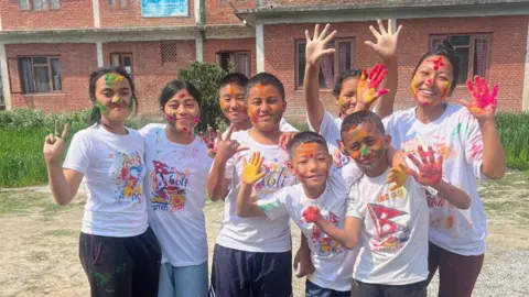 Eight children in white t-shirts with brightly coloured Holi paint on their hands and faces