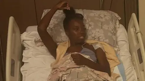 Chenai Johnson in a hospital bed in Egypt. She is awake and looking to one side. 