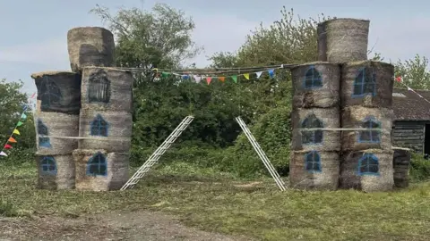 March Young Farmers Two stacks of straw bales, painted with windows, and two ladders in between, recreating Tower Bridge, London