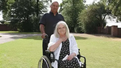 Family handout An elderly woman in a wheelchair with a middle-aged man standing behind her