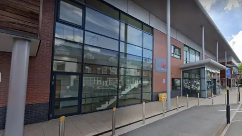 A wide brick building with several glass panels by the side of a road.