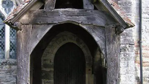 Richard Dunn The entrance of the church which has some damage on it. There is grass in front of it. 