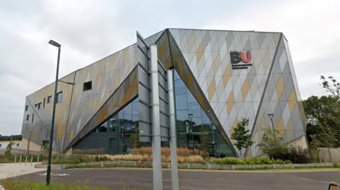 Google Building on Bournemouth University campus, which has an angular design with silver and gold panelling. A pink and black 'BU' logo is on the side of the building.