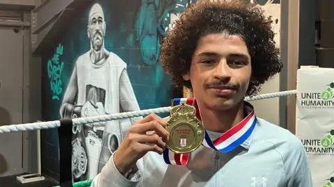 Shariqua Ahmed / BBC Ismael wearing a grey track suit with a gold medal around his neck