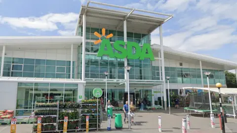 Entrance to Asda with big green Asda sign, and shoppers walking with trollies.