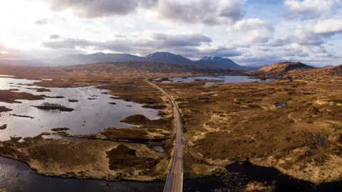 An aerial view of a road crossing Rannoch Moor. The moor is a vast expanse of peat moorland and lochs