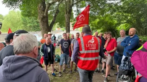 Steve Preddy People are gathered round a man facing away from the camera in a red Unite jacket and holding a flag