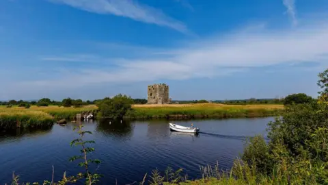 Lee Haggarty A small boat in the River Dee halfway across to the island on which the imposing Threave Castle stands