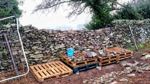 Stone wall with wooden pallets in front of it.