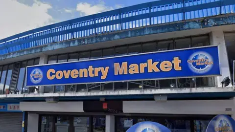 A large blue sign on a grey building which reads Coventry Market in yellow lettering