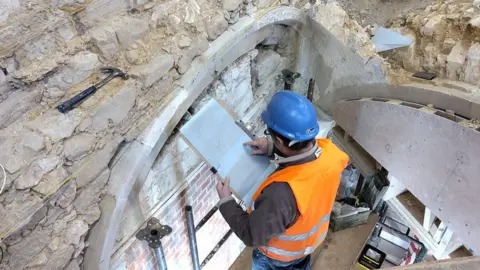 A man wearing a hard hat and high-vis jacket recording the medieval undercroft at Priory House