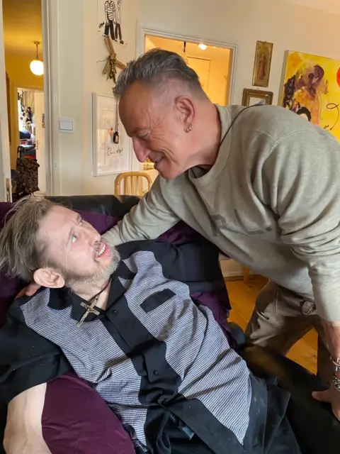 Victoria MacGowan / Twitter Bruce Springsteen embraces Shane MacGowan, who is resting on a sofa, looking frail. 
