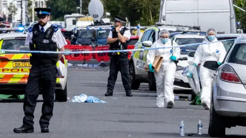 PA Media Police on Hart Street Southport - Police officers in uniform and forensic white suits in the street behind a cordon with emergency vehicles