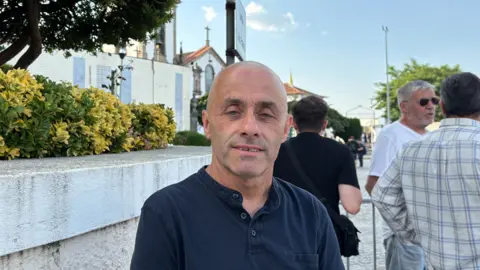 Sofia Ferreira Santos/BBC A bald man standing in front of a white church