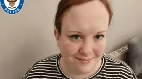 Family handout A young woman with red hair, tied back, and brown eyes smiles into the camera. She has eyeliner which flicks at the side and is wearing a stripey t-shirt