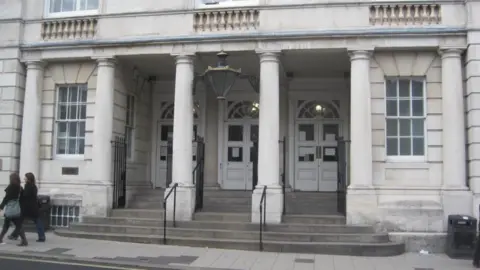 A court building. The court building is made of white brick and has pillars in front of three white doors.