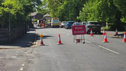 A red 'road closed' sign with cones blocking the road.