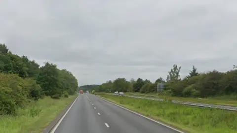 Google Google Streetview of a northbound stretch of the A1 in Nottinghamshire. The dual carriageway is surrounded by trees on one side and a grass verge in the other. Vehicles are driving in the distance.