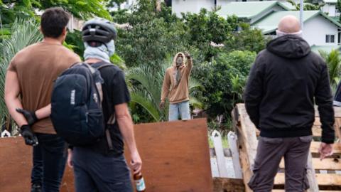 Masked residents watch an activist at the entrance to Tuband, in the Motor Pool district of Noumea