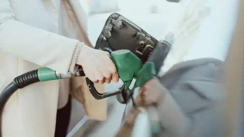 A woman's hand putting fuel in her car using a green fuel pump.