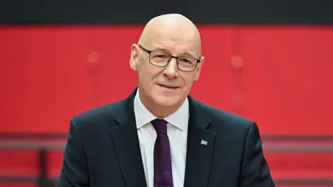 Reuters John Swinney smiling at the camera. He is wearing a suit. 