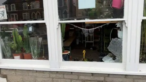 Pepe Cactus Photograph of the outside of Pepe Cactus store in Corp Market, Canton. The middle window of the store is pictured completely smashed through, with shards of glass remaining on the perimeter of the window frame. In the window to the left, several cactus plants can be seen on the window sill. 