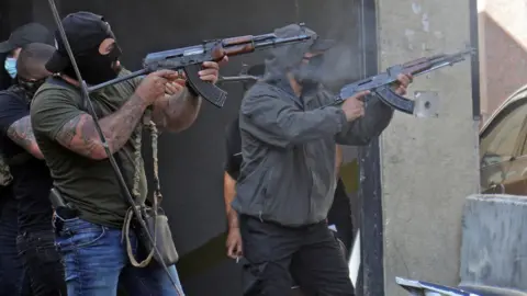 Getty Images Shia fighters from Hezbollah and Amal movements take aim with Kalashnikov assault rifles amidst clashes in the area of Tayouneh, in the southern suburb of the capital Beirut, on October 14, 2021