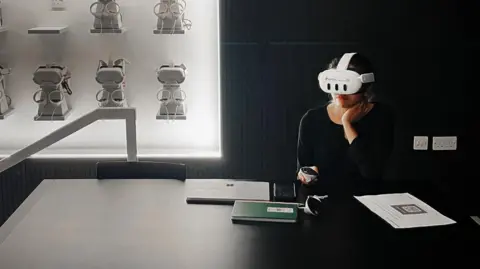 Revolve Labs A woman in a black room wearing a VR headset while sitting at a table. 