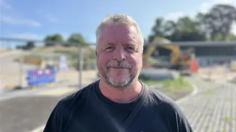George Carden/BBC John Bownas, manager of Love Hastings, pictured near the A21 roadworks. He has greying hair and is wearing a black t-shirt.