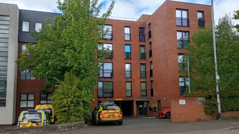 A red brick building with trees and a police car outside it