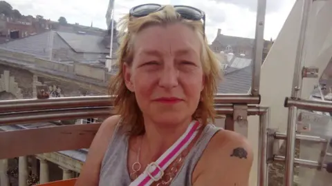 Facebook 44-year-old Dawn Sturgess is seen smiling on a balcony, wearing a gray vest, a shoulder bag and sunglasses on her head.