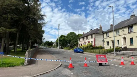 Scene of incident in Aberdeen with road closed sign and police tape.